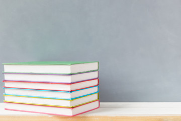 stack of multicolour books on a wooden shelf and gray wall. with copy space