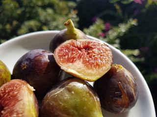 Fresh figs in a bowl close up. Tropical fruit on green outdoor background.