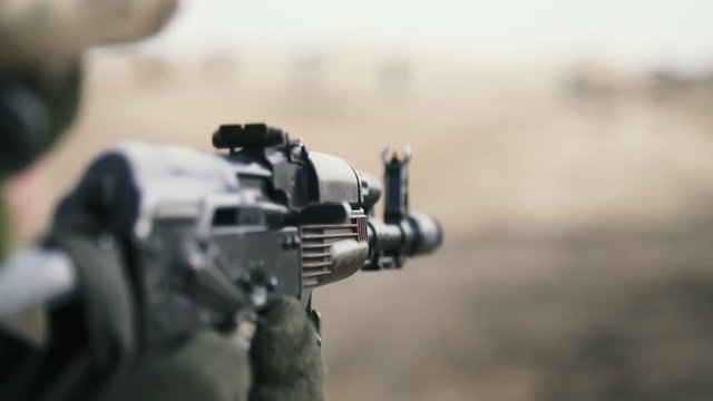 Soldier shooting from AK 74 in a khaki uniform in a field in slow motion