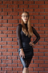 Elegant smiling woman in eyeglasses on a brick wall background