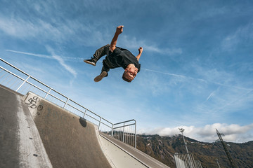 Young Parkour and Freerunning athlet doing a backflip from a wall in an urban enviroment with a blue sky in de background, jumping tumbling  Gymnastics training concept