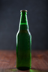 Beer in a green bottle with water drops on wooden table on dark background.