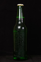 Beer in a green bottle with water drops on wooden table on dark background.