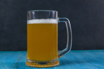 Mug of beer on wooden table on dark background