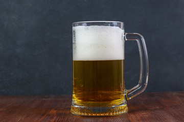 Beer in a mug with water drops on wooden table on dark background.