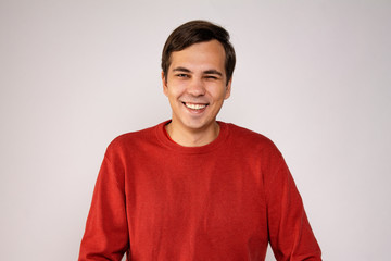 A young guy in a red sweater laughs. Portrait on light background
