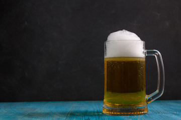Mug of beer on wooden table on dark background