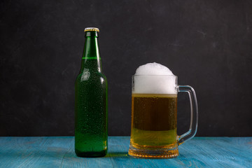 Mug of beer and green bottle with beer on wooden table on dark background