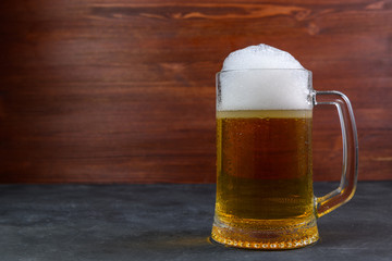 Beer in a mug with water drops on wooden table on dark background.