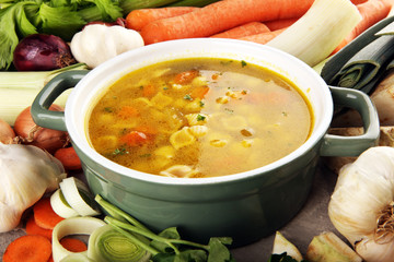 Broth with noodles and carrots, various fresh vegetables in a pot - colorful fresh clear spring soup. Rural kitchen scenery vegetarian bouillon stock