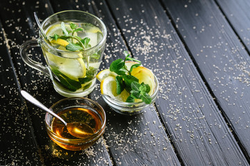 Fresh ginger tea with lemon slices, mint and honey on a dark background.