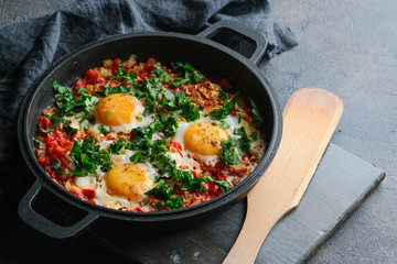 Traditional  shakshuka with eggs, tomato, and parsley in a iron pan on a dark background