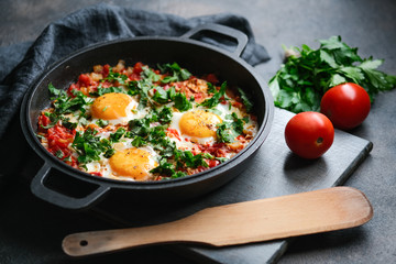 Traditional  shakshuka with eggs, tomato, and parsley in a iron pan on a dark background