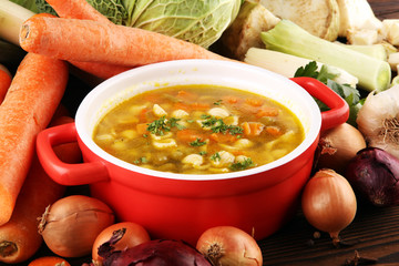 Broth with noodles and carrots, various fresh vegetables in a pot - colorful fresh clear spring soup. Rural kitchen scenery vegetarian bouillon stock