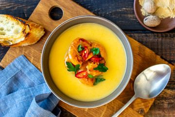 Cheese cream soup with grilled shrimp on a wooden background.