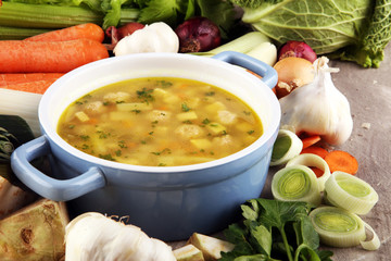 Broth with marrow dumplings and carrots, onions various fresh vegetables in a pot - colorful fresh clear spring soup. Rural kitchen scenery bouillon