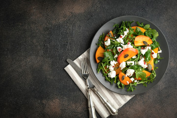 Healthy salad with persimmons, arugula, feta cheese and pumpkin seeds on a dark plate on a dark background. Vegetarian menu, healthy food. Prevention of vitamin deficiency. Top view.