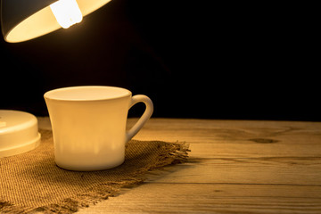 A cup of coffee resting on a table with a reading lamp paired together