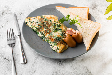 Omelet with spinach, sausages and sourdough toast isolated on white marble background. Homemade food. Tasty breakfast. Selective focus. Hotizontal photo.