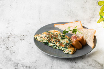 Omelet with spinach, sausages and sourdough toast isolated on white marble background. Homemade food. Tasty breakfast. Selective focus. Hotizontal photo.