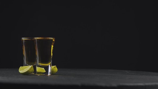 two glasses with golden tequila on a black background on a rotating black board. Coarse salt falls on top of tequila. alcoholic drinks at the bar. Close-up shot. 4k video. 59.94 fps
