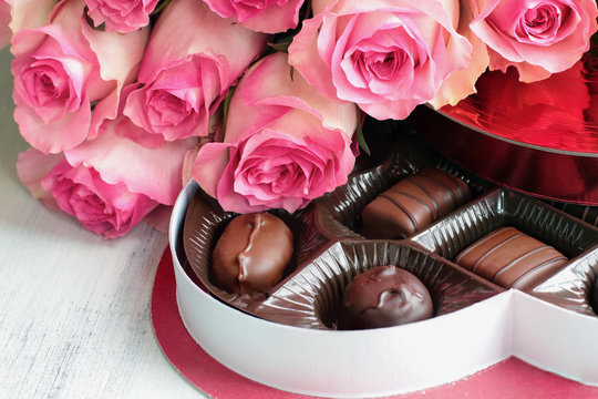 Dozen soft colored long stem pink rose flowers with a heart shaped box of chocolate candy for Valentine Day over a wood background.