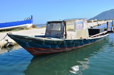 Fototapeta na wymiar Lefkada, Lefkada Island, Greece. 10/22/2019. old, broken wooden ship blue, white and red color, fishing boat on the water in the port on the pier
