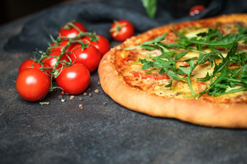 Traditional Italian pizza with ham, arugula, mozzarella, basil and tomatoes on a dark background copy space.