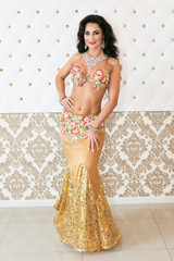 Oriental dancer in a golden dress. Woman brunette belly dancer in a luxurious interior
