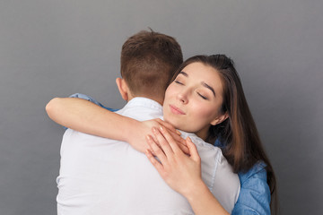 Relationship Concept. Young couple hugging woman smiling delightful studio standing isolated on grey