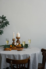 Christmas table in Scandinavian interior. Candles in wooden candlesticks, fresh spruce branches, champagne and gingerbread on an authentic textile tablecloth. Round table, copy space