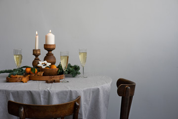 Christmas table in Scandinavian interior. Candles in wooden candlesticks, fresh spruce branches, champagne and gingerbread on an authentic textile tablecloth. Round table, copy space