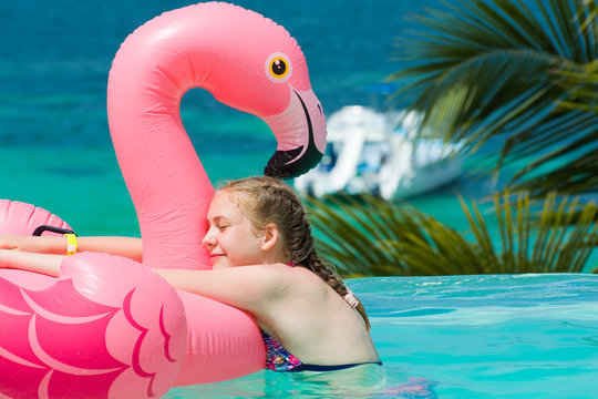 Caucasian teenage girl hugging her inflatable pink flamingo in infinity swimming pool in luxury hotel, Punta Cana, Dominican Republic. Summer vacation concept