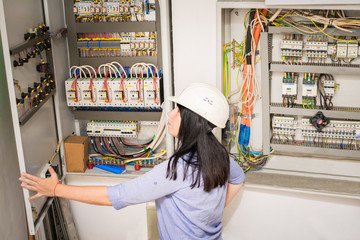The specialist works in the electrical distribution panel. Female engineer in white helmet switches on circuit breakers in electrical box. Professional girl checks the switchboard of the enterprise.
