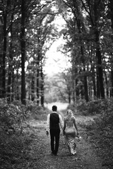 Obraz premium Black and white foto the newlyweds walk hand in hand along the path in the forest. Back view. Bride and groom enjoying romantic moment together on wedding day. The concept of youth, love and lifestyle