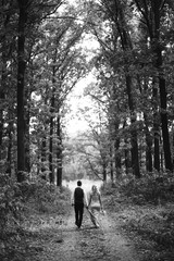 Obraz premium Black and white foto the newlyweds walk hand in hand along the path in the forest. Back view. Bride and groom enjoying romantic moment together on wedding day. The concept of youth, love and lifestyle
