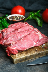 Fresh raw beef, cut into steaks on a wooden board with vegetables, herbs and spices on a wooden board on a dark background.