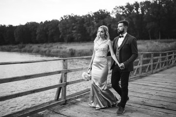 Black and white foto stylish couple of newlyweds posing on a bridge on wedding day. Handsome bearded groom admires and kisses pretty bride. Together. The concept of youth, love, fashion and lifestyle.