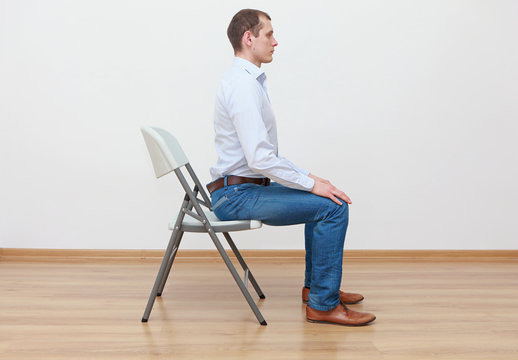 caucasian man sitting on the edge of chair in correct  posture