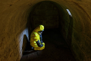  Man in protective uniform, gas mask,gloves, boot in dark tight shelter