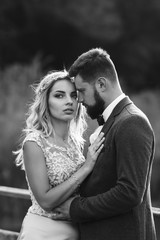 Black and white foto stylish couple of newlyweds posing on a bridge on wedding day. Handsome bearded groom admires and kisses pretty bride. Together. The concept of youth, love, fashion and lifestyle.