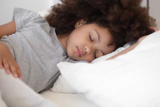 Calm little biracial girl sleeping peacefully in white bed