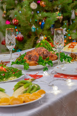 Fototapeta na wymiar Festive Christmas served table against beautiful green pine tree decorated with many colorful new year toys. Xmas dinner, delicious food, christmas turkey. Winter holidays celebration at cozy home