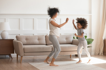 Happy biracial mom and daughter dancing together at home