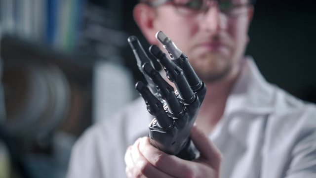 A scientist engineer is testing an electronic bionic prosthetic arm. He moves the plastic fingers of a mechanical arm. Modern technologies in prosthetics. Cybernetic hand in the hand of a scientist.