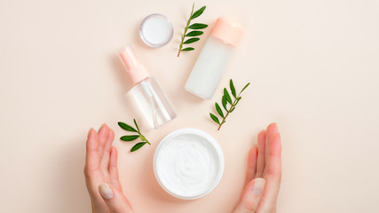 Jar of organic hand cream, essential oils bottle and green leaves on beige background. Skin care,...