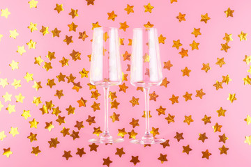 Two empty champagne glasses on a pink pastel background surrounded by golden stars.