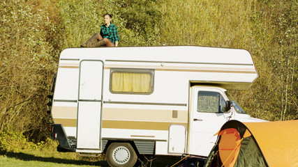 Young girl relaxing on top of retro camper van in mountain wilderness