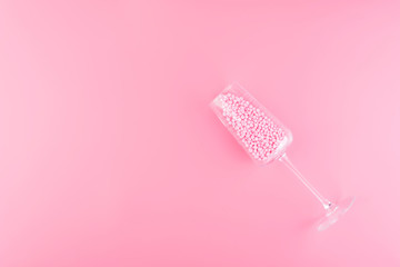 A glass of champagne is filled with decorative balls a pink pastel background.