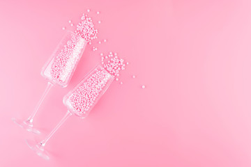 Two glasses of champagne is filled with decorative balls a pink pastel background.